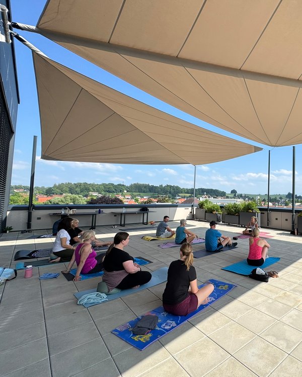 Eine Gruppe Menschen, die auf Yogamatten, auf der Dachterasse der RÖSLE Kochschule sitzen. | © RÖSLE GROUP